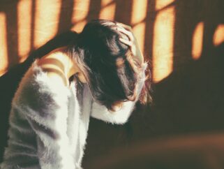 woman leans on wall in white fur jacket docking her head while holding it using her leaf hand