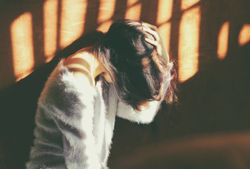 woman leans on wall in white fur jacket docking her head while holding it using her leaf hand