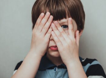 child hiding his face behind fingers