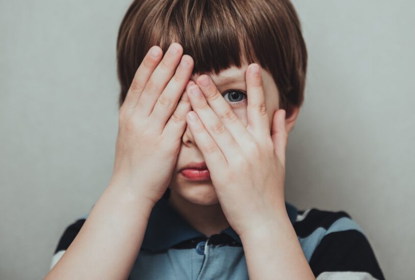 child hiding his face behind fingers
