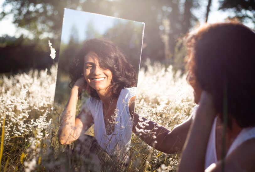 Selbstwarhrnehmung: Frau sitzt mit Spiegel im Gras